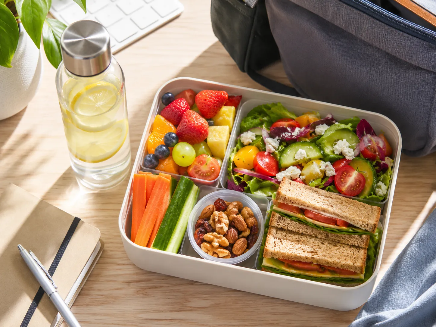 Kleurrijke lunchbox met salade, fruit, groente, noten en een volkoren sandwich voor werk, school of onderweg.